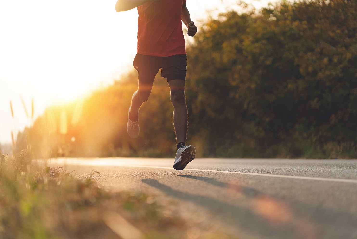 Guy running into the sunset on a country road with bushes either side