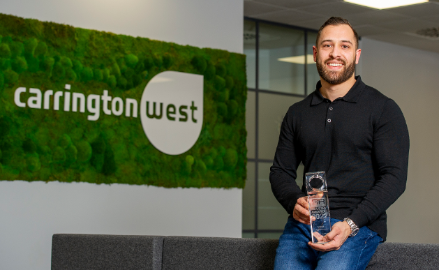 Cameron De Wit, Lead Consultant in Town Planning, sitting proudly holding their Temporary Recruiter of the Year Award with the Carrington West logo in the background.