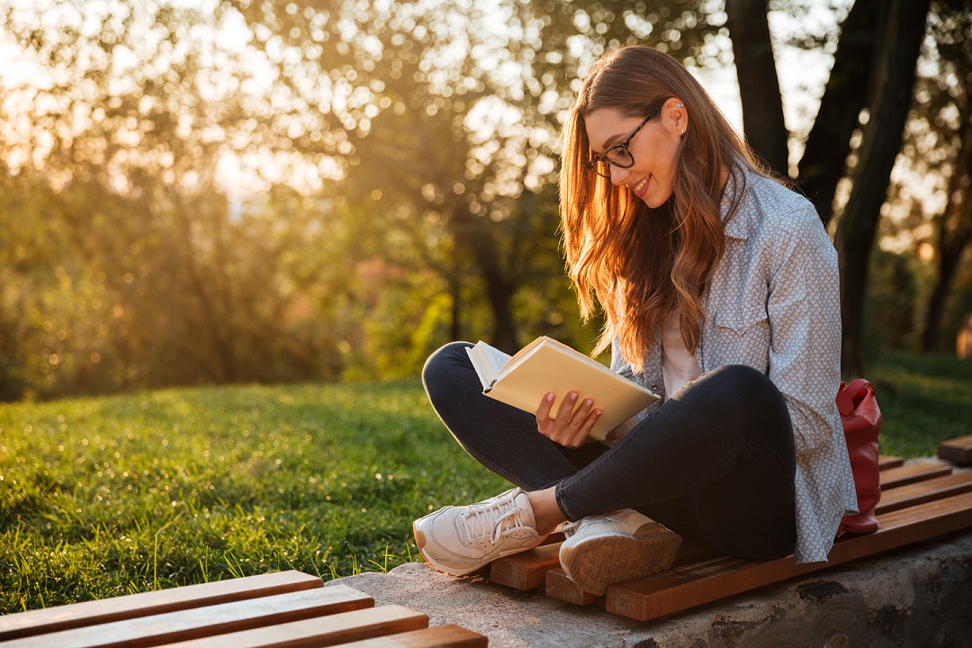 Woman sitting in the park reading a book during sunset