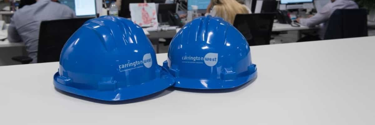 Two Carrington West branded hard hats on an office desk